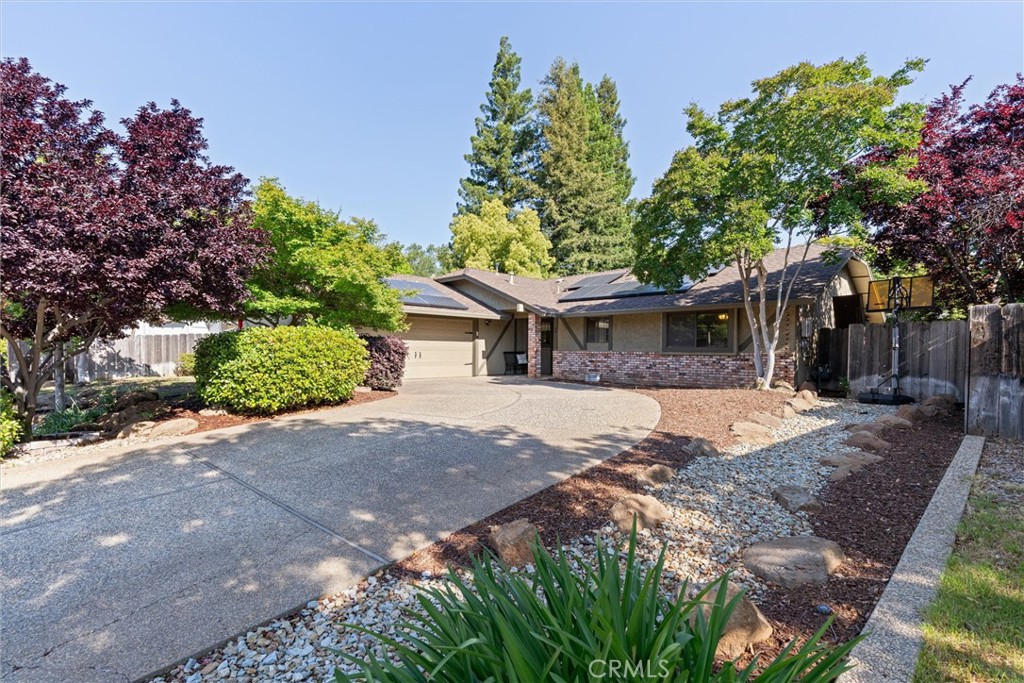 Single-story home with solar panels, brick facade, and a curved driveway shaded by mature trees.