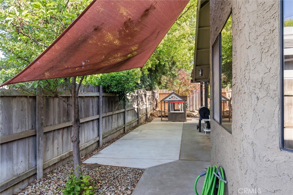 Side patio with a rust-colored shade canopy, wooden fence, and small playhouse.