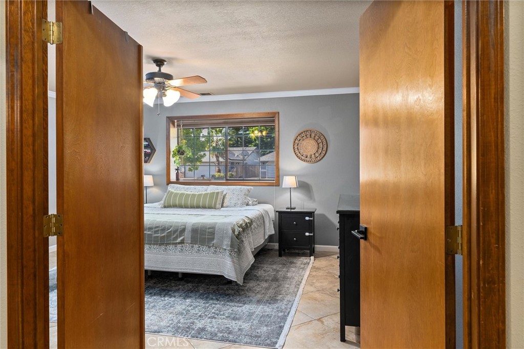 Furnished bedroom with open wooden doors, a large window, and a ceiling fan.