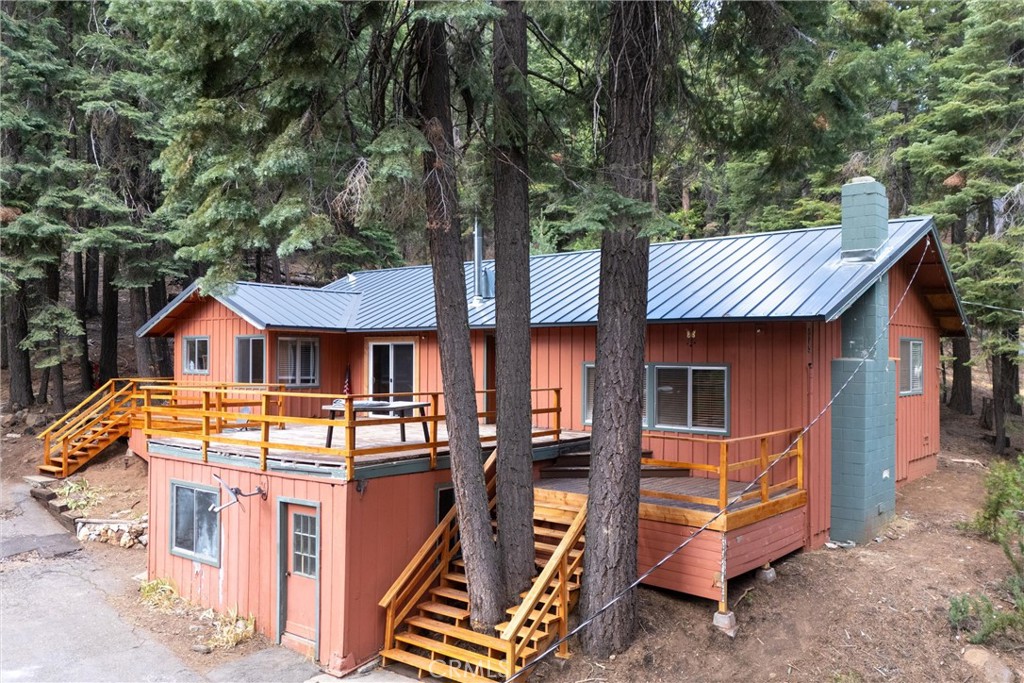 Two-level cabin with elevated wooden decks and stairs among tall evergreen trees.