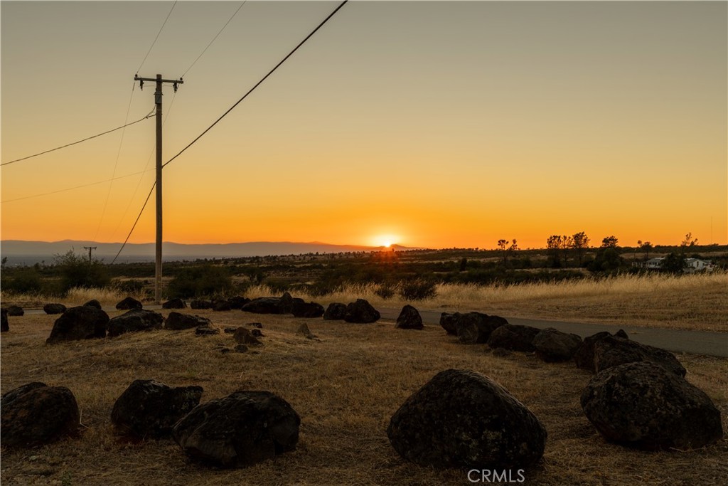 Dry, rocky rural landscape at sunset, with a utility pole and distant hills.