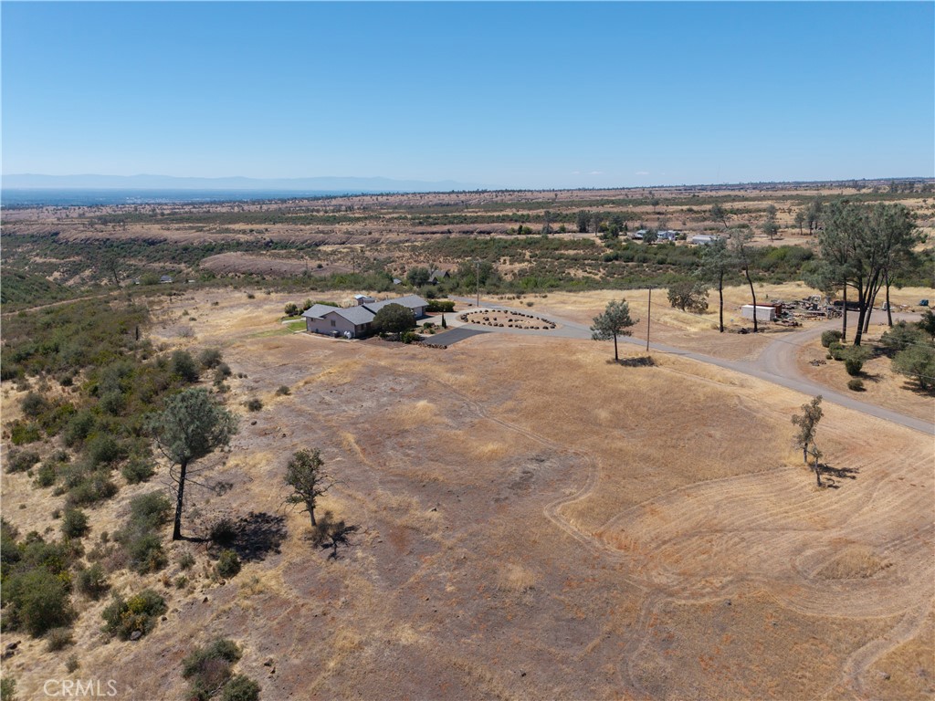 Aerial view of a rural home and outbuildings on a large dry lot with a curved driveway.