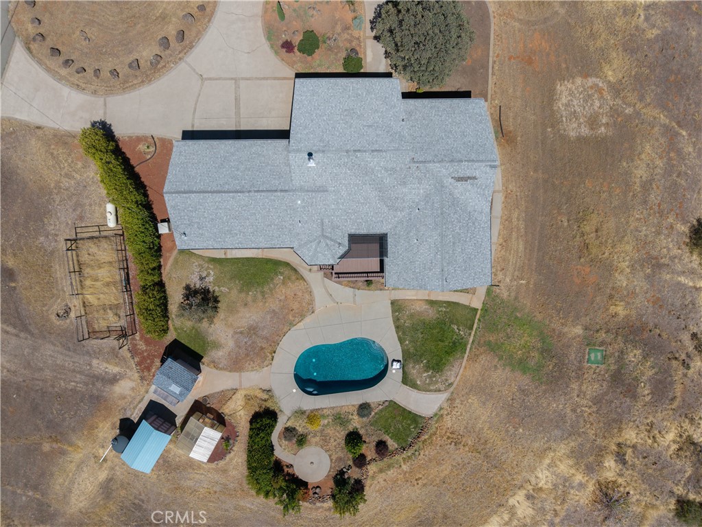Aerial view of a home with a gray roof, oval pool, and curved walkways.