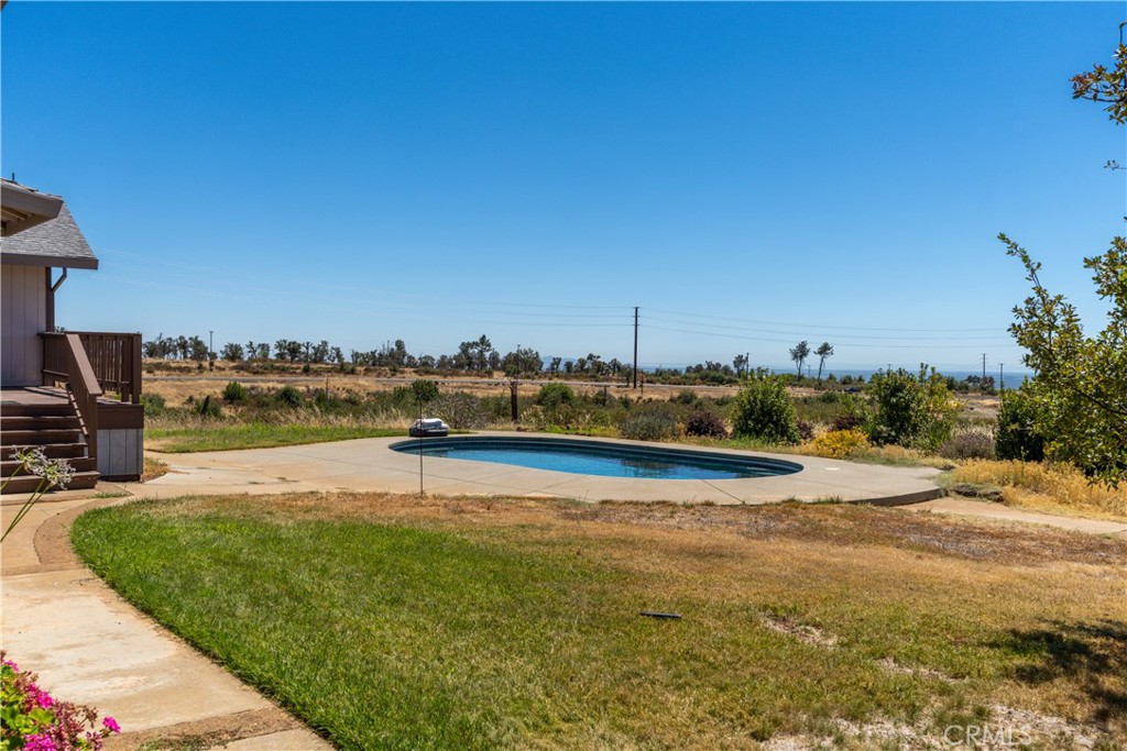 Outdoor swimming pool beside a concrete patio and dry lawn, with open fields in the distance.