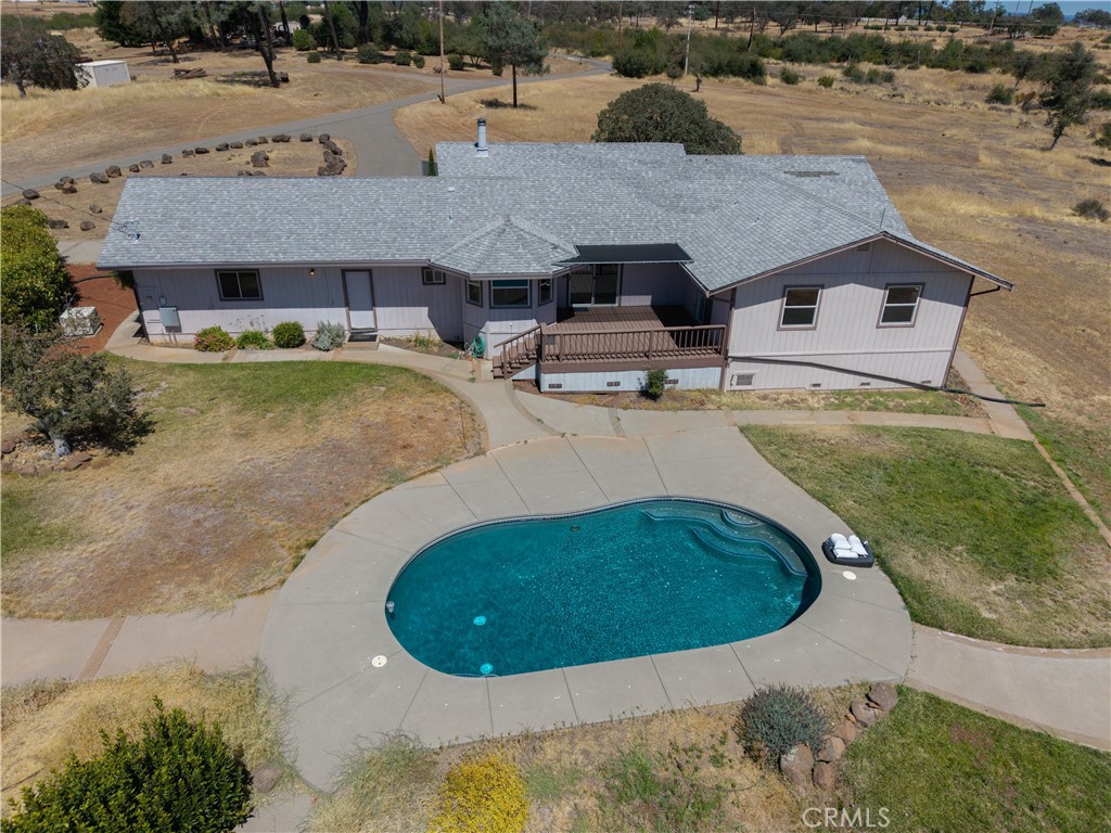 Aerial view of a single-story home and swimming pool, with a raised wooden deck and curved driveway.