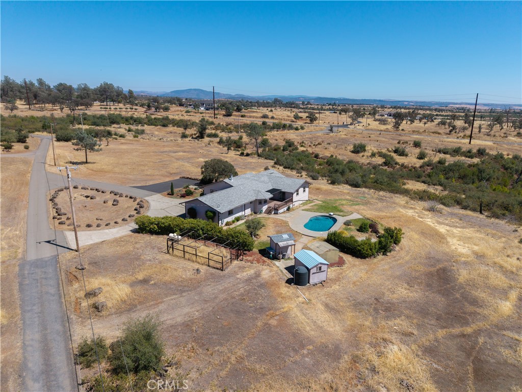 Aerial view of a rural home with a turquoise pool, outbuildings, and dry open land.