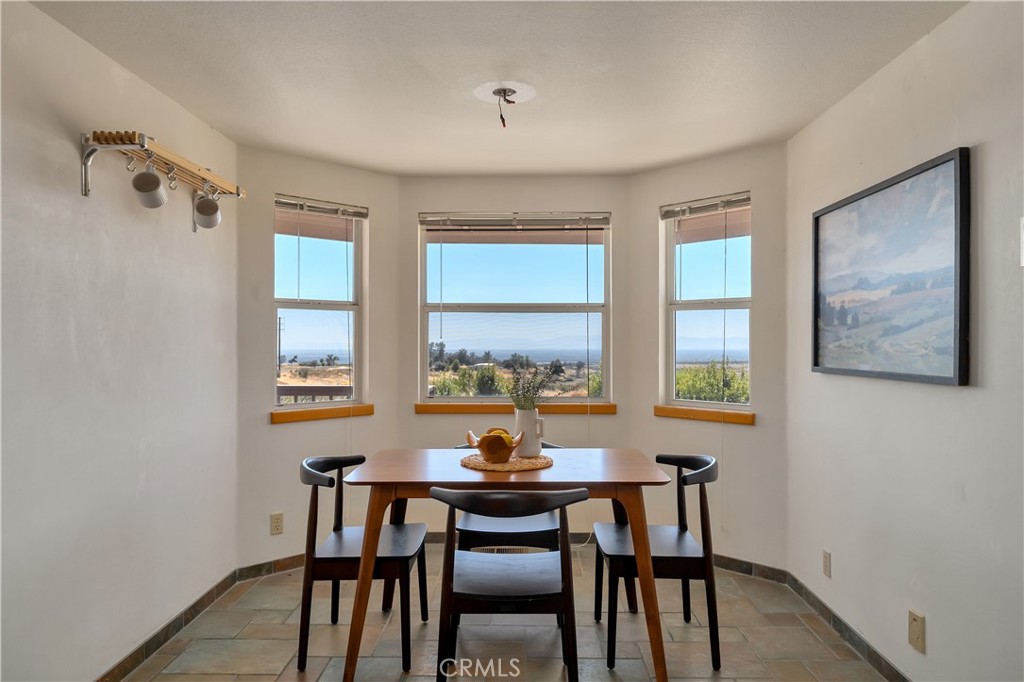 Dining area with a wooden table and black chairs beneath three windows overlooking the landscape.