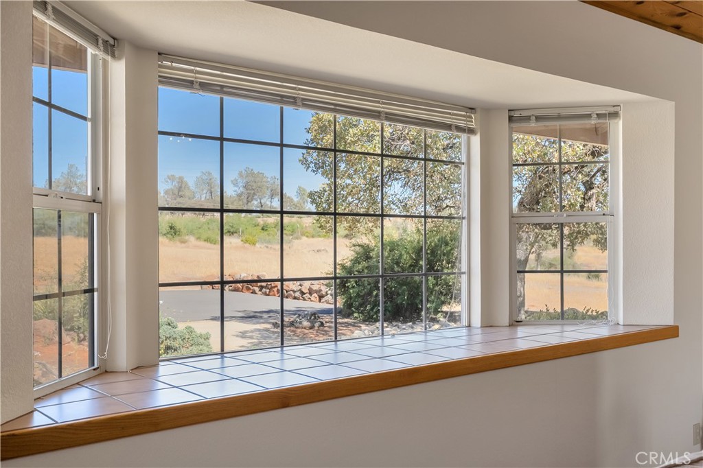 Interior window wall with tiled sill overlooking a dry, tree-dotted landscape.