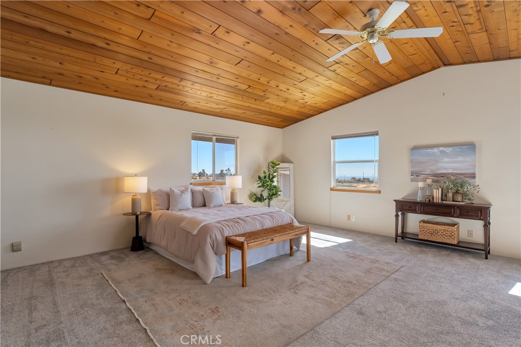 Staged bedroom with a king-size bed beneath a vaulted wood-plank ceiling and ceiling fan.