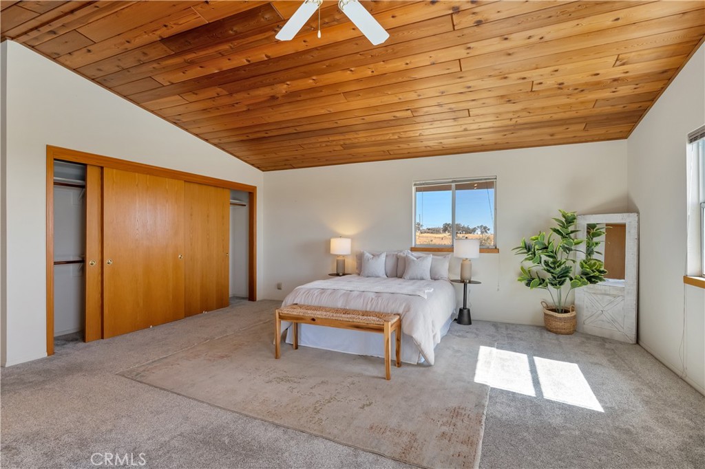 Bedroom with a white bed beneath a distinctive wood plank ceiling and broad sliding closet doors.