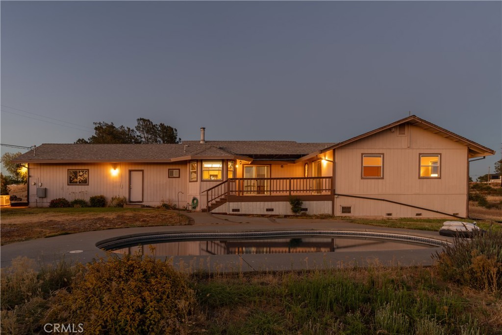 Single-story home at dusk with glowing windows and a curved pool in front.