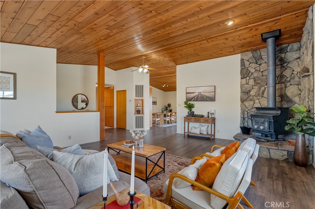 Living room with a vaulted wood ceiling, stone fireplace, and adjoining dining area.