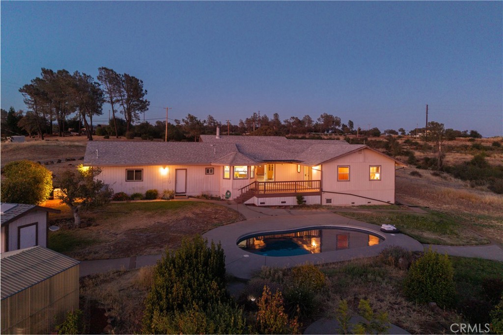 Ranch-style home with a curved swimming pool at dusk, viewed from the backyard.