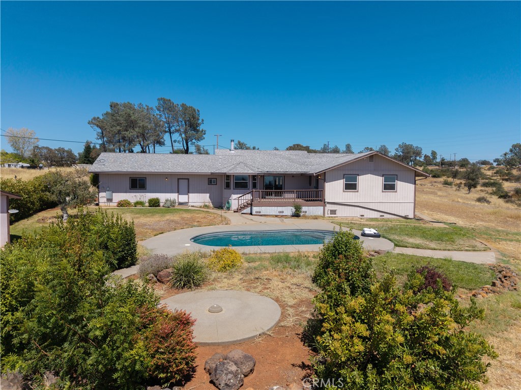 Rear of a single-story home with a raised deck, swimming pool, and landscaped yard.