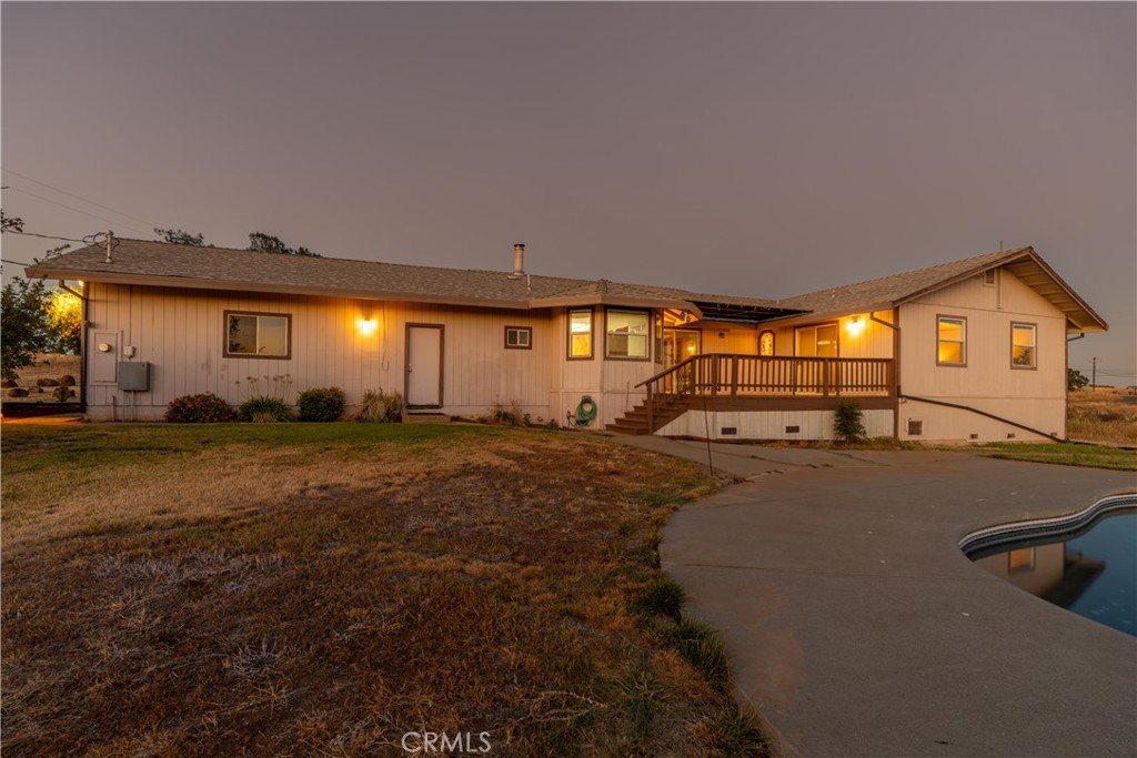 Single-story home at dusk with a raised wooden deck and a swimming pool in the foreground.