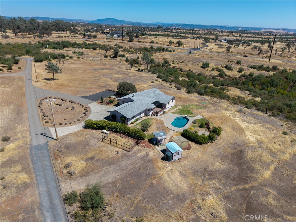Aerial view of a rural home with a turquoise swimming pool, outbuildings, and distant hills.