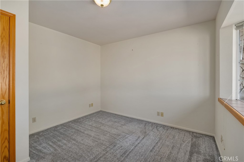 Empty carpeted room with white walls, a wooden door, and a wood-trimmed window.