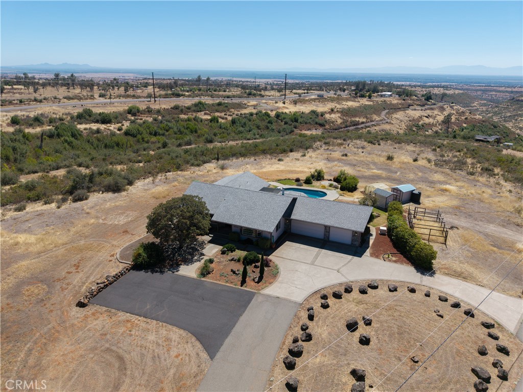 Aerial view of a ranch-style home with a pool, circular driveway, and dry open land.