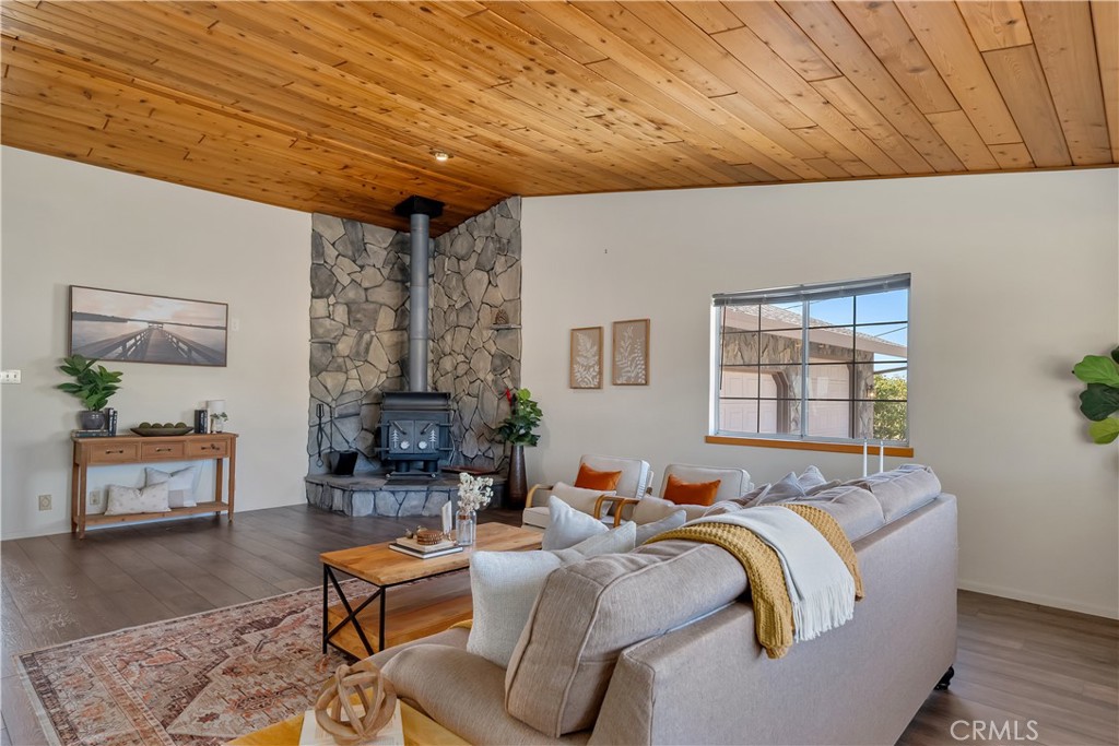Living room with a stone fireplace and wood stove beneath a warm wood-plank ceiling.