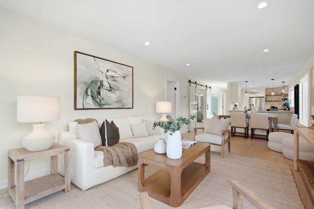 Staged living room with a white sofa and wood coffee table, opening to the dining area and kitchen.