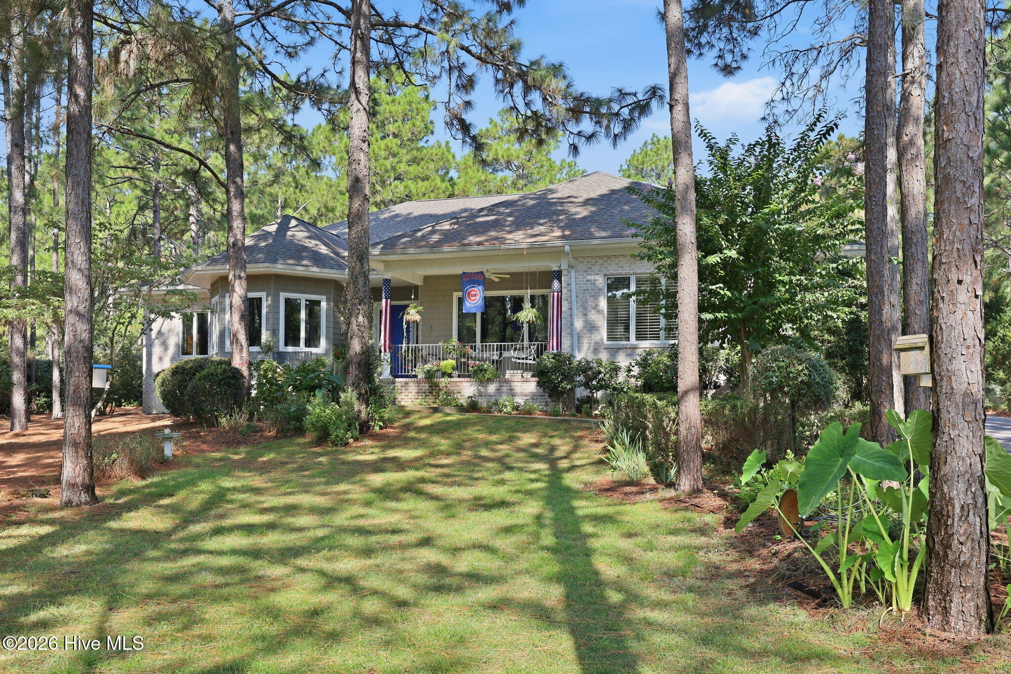 Gray home with a covered porch nestled among tall pine trees and a sunlit lawn.