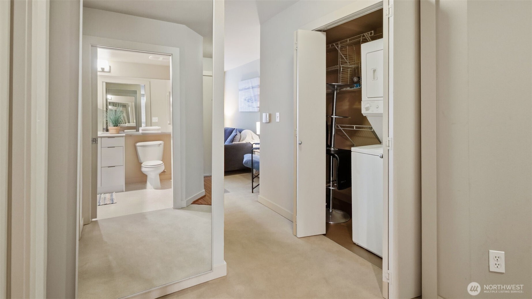 Condo hallway with mirrored wall, bathroom doorway, and open laundry closet.