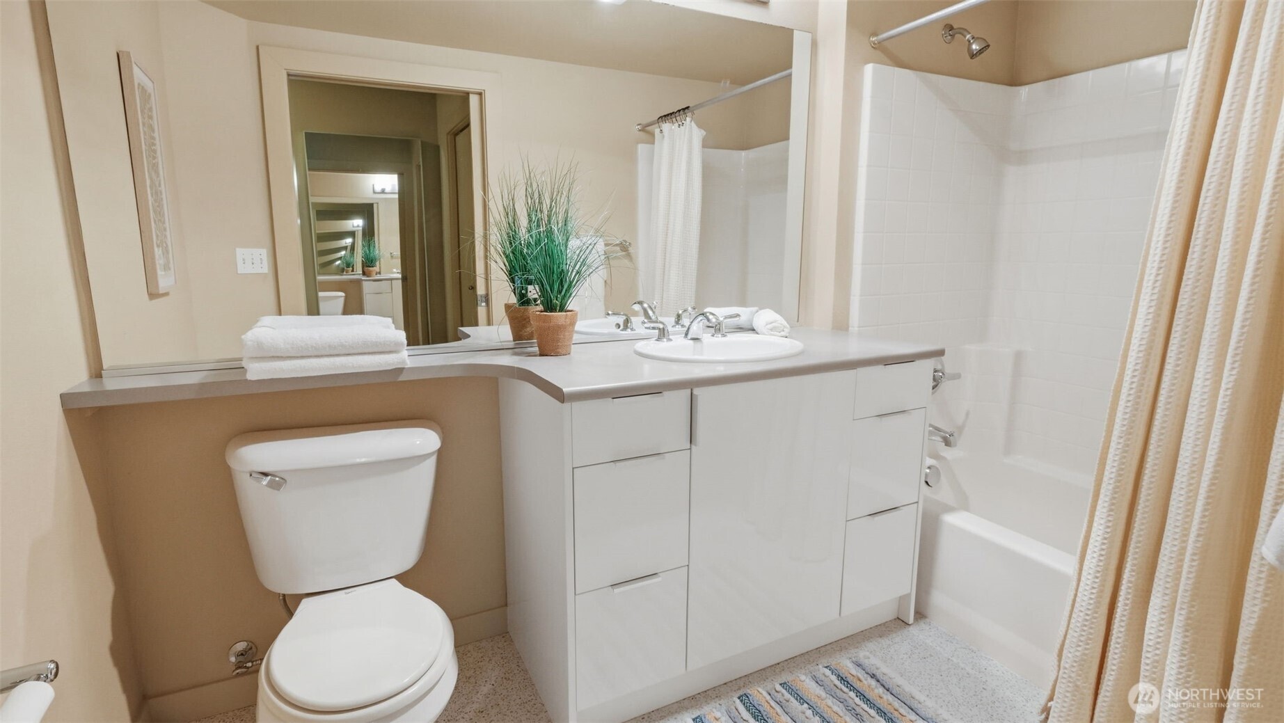 Bathroom with a long white vanity, large mirror, toilet, and white-tiled tub.