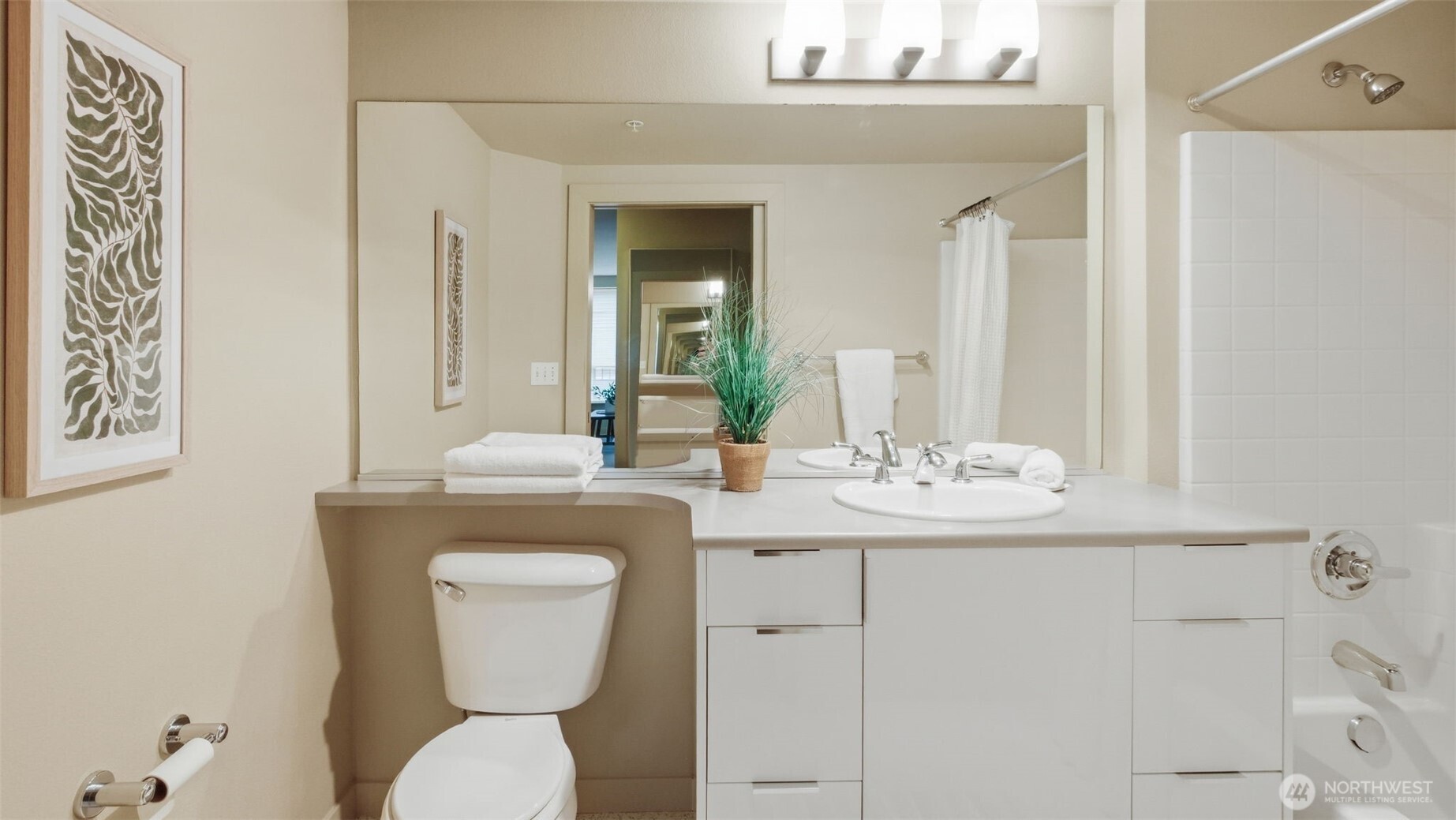 Bathroom with a long white vanity and mirror, toilet, and tiled tub-shower.