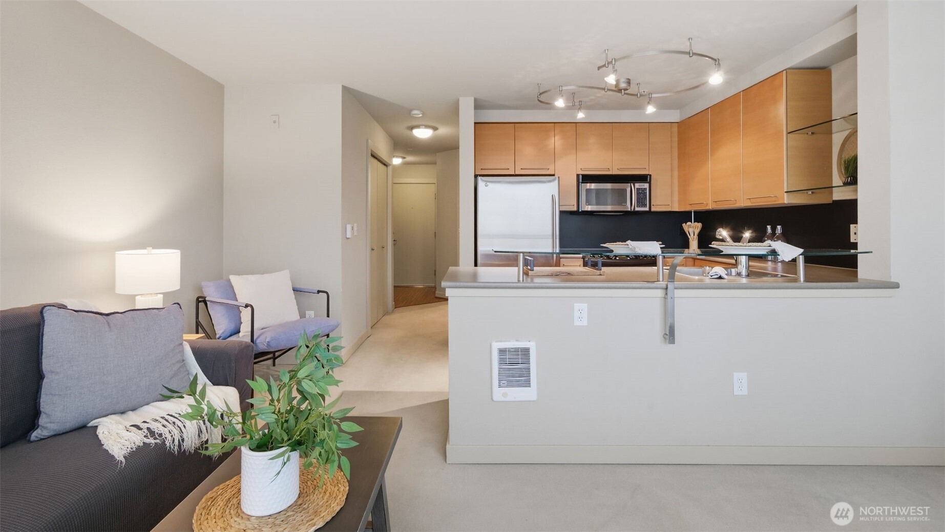 Open-plan condo kitchen with wood cabinets and breakfast bar beside a staged living area.