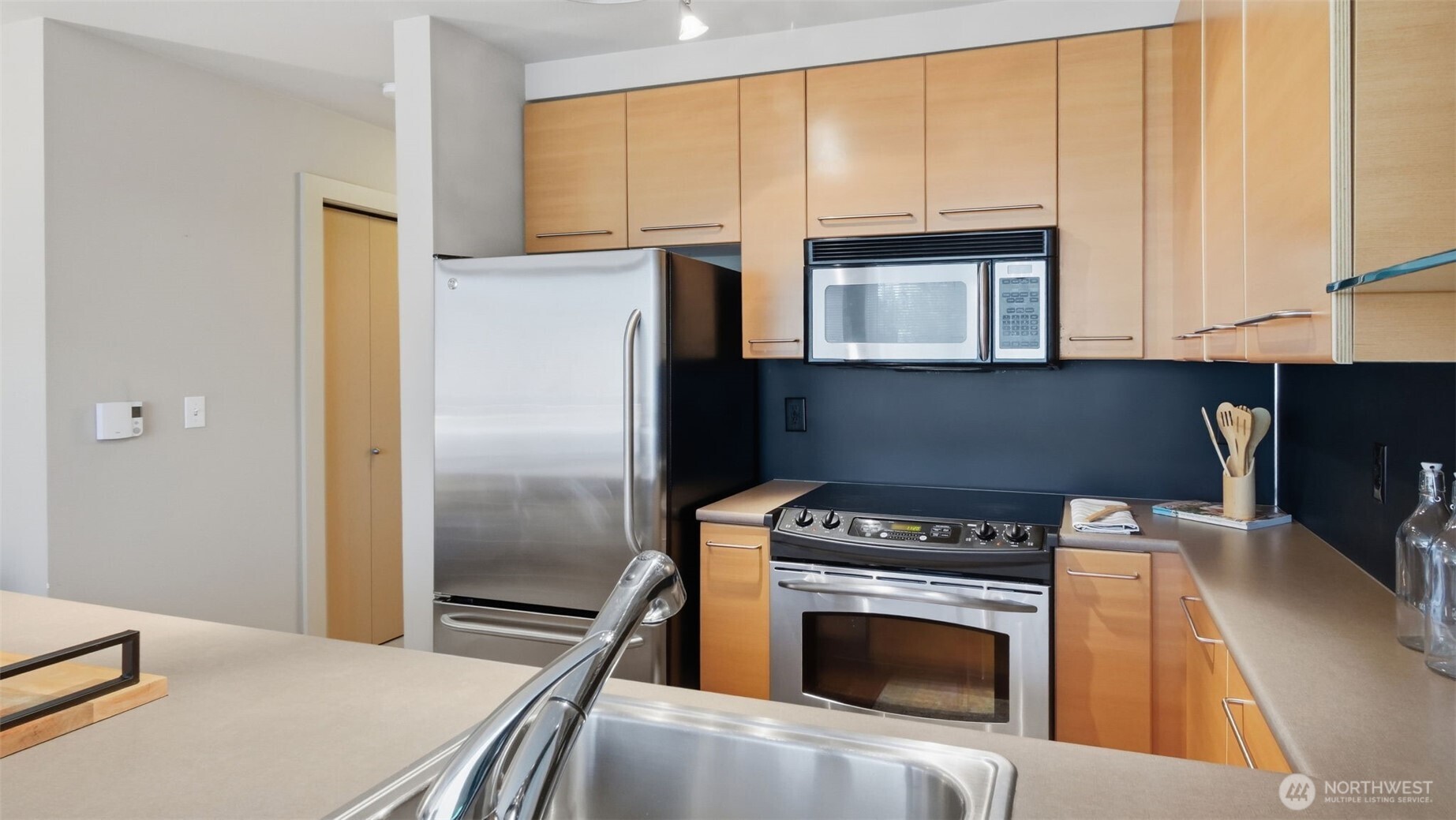 Kitchen with light wood cabinetry, dark backsplash, and stainless steel appliances.