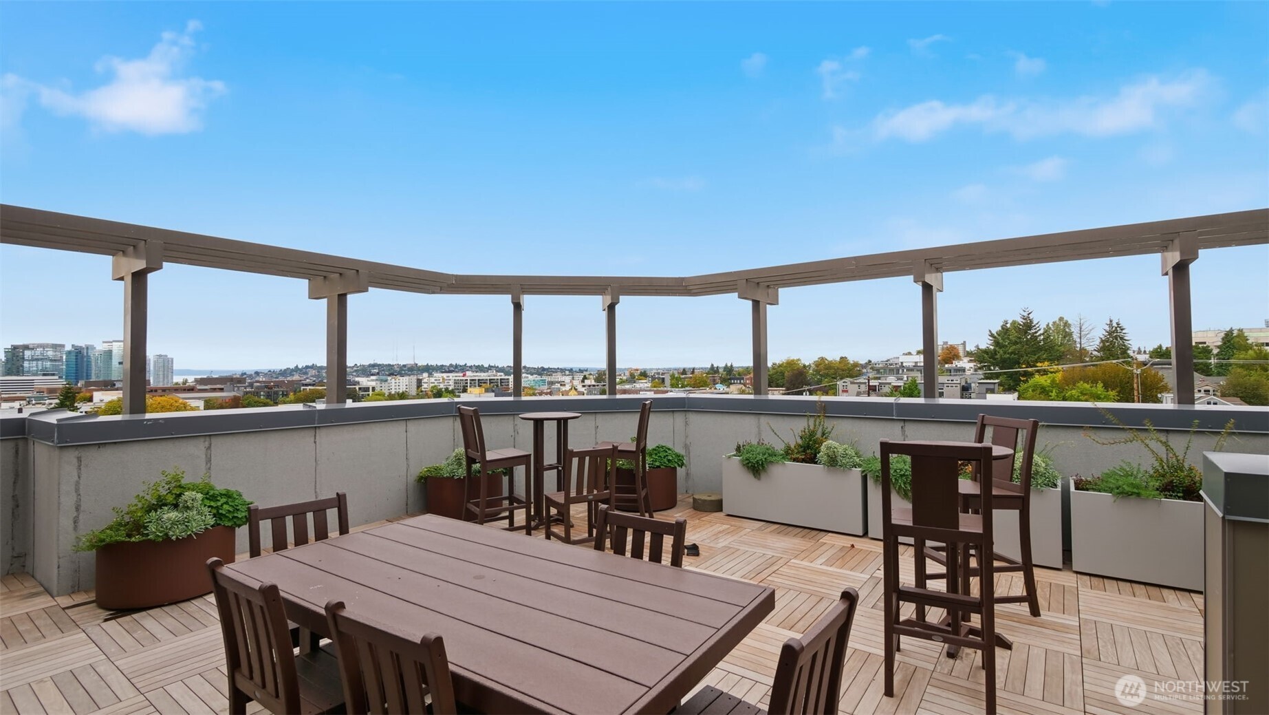 Rooftop terrace with outdoor dining furniture, wood decking, and planters overlooking the city.