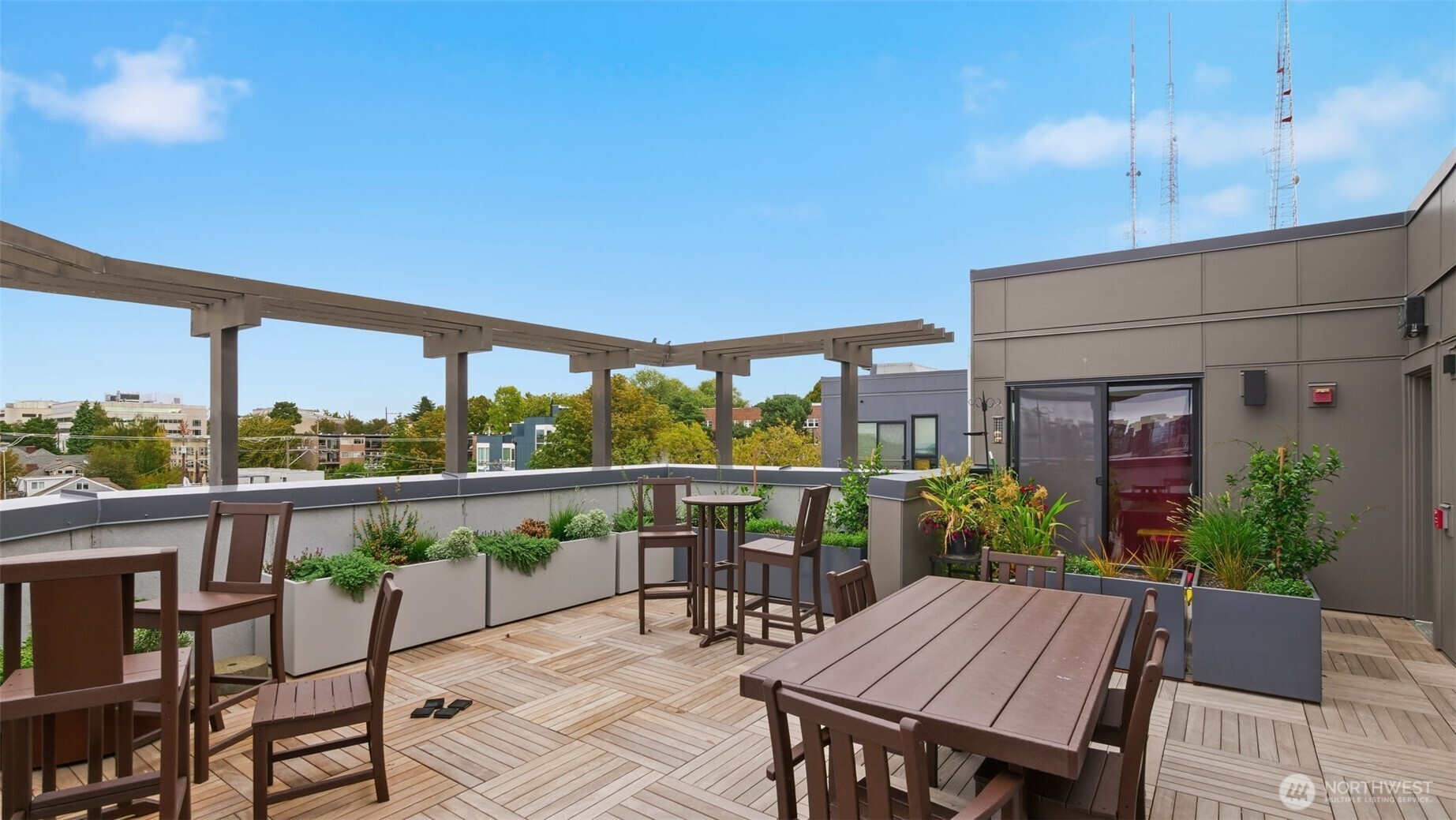 Rooftop terrace with wood decking, dining furniture, planters, and a pergola.