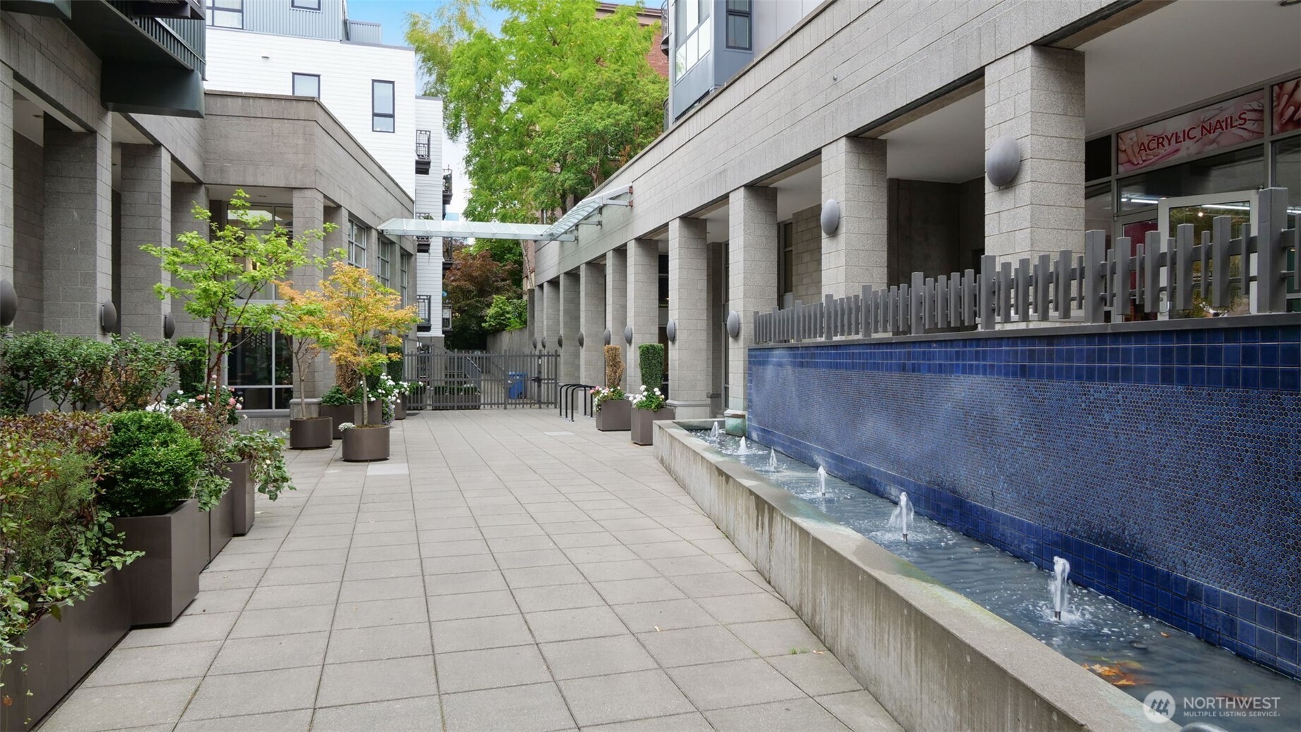 Apartment courtyard with potted trees and flowers beside a long blue-tiled fountain.