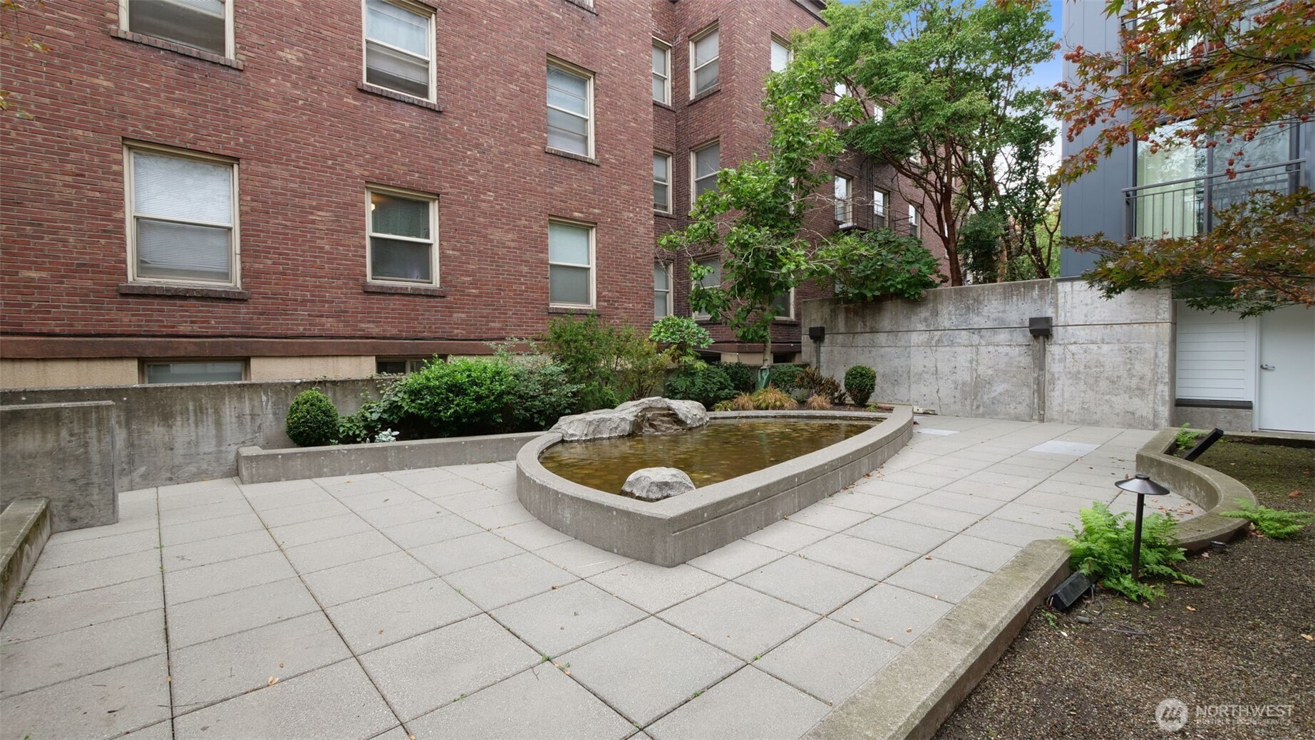 Apartment courtyard with a raised reflecting pool, brick building, and landscaped planting beds.