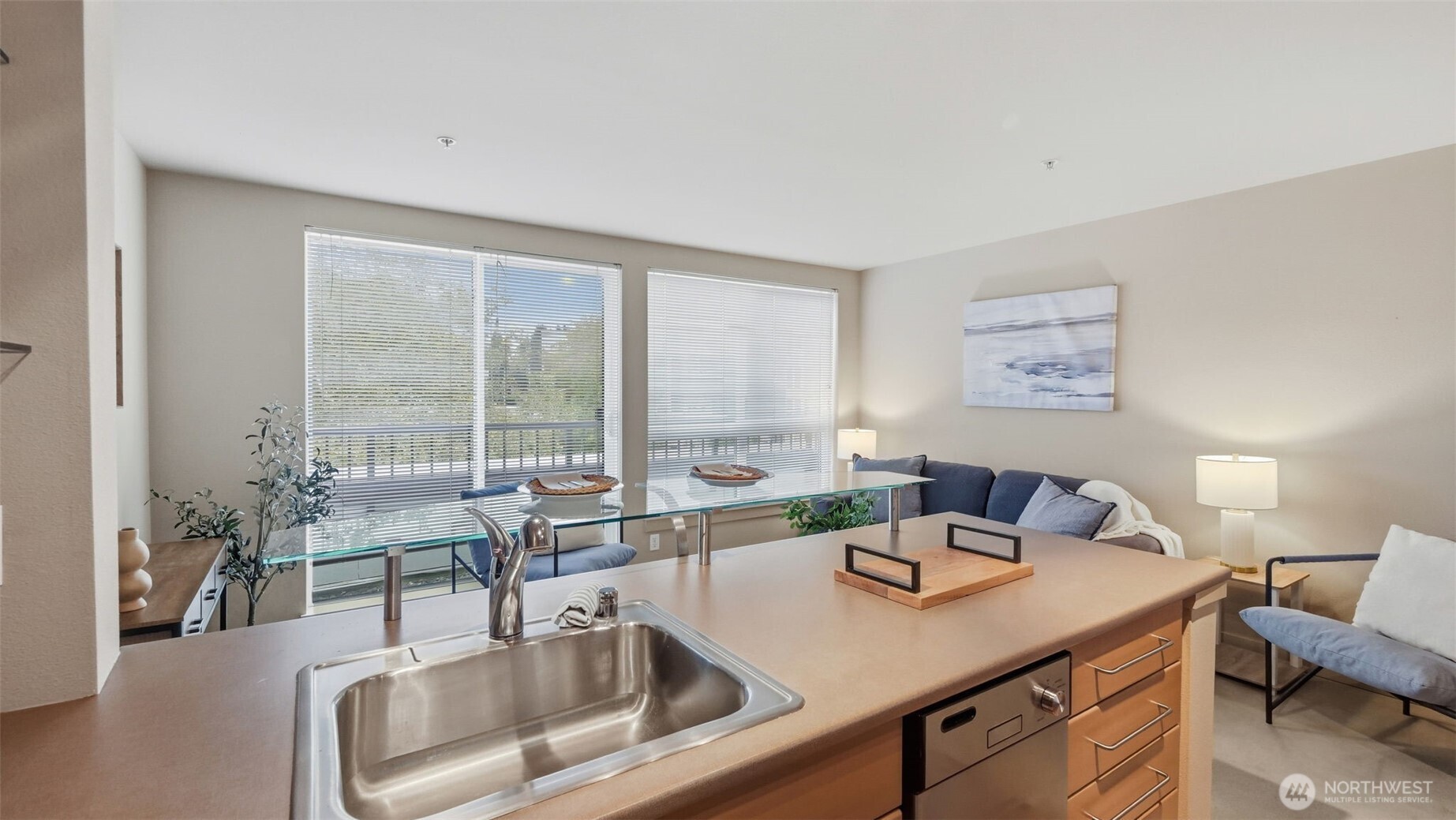 Open-plan condo kitchen with a large island and stainless-steel sink facing a furnished living area.