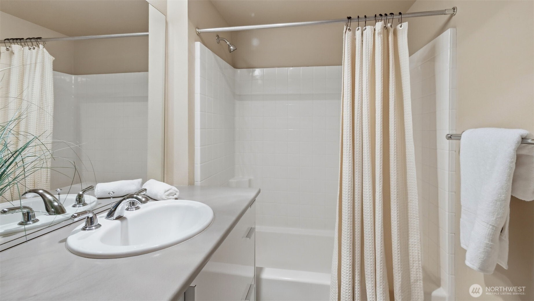 Bathroom with a white tiled tub and shower, curtain, and vanity with an oval sink.