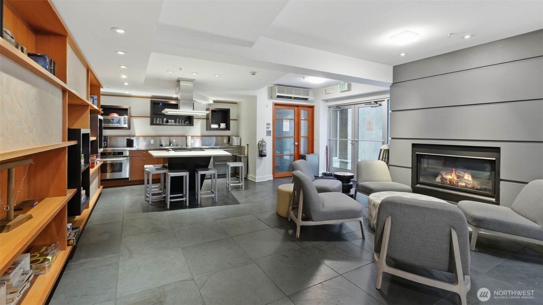 Furnished condo lounge with kitchenette, built-in shelves, gray seating, and a lit fireplace.