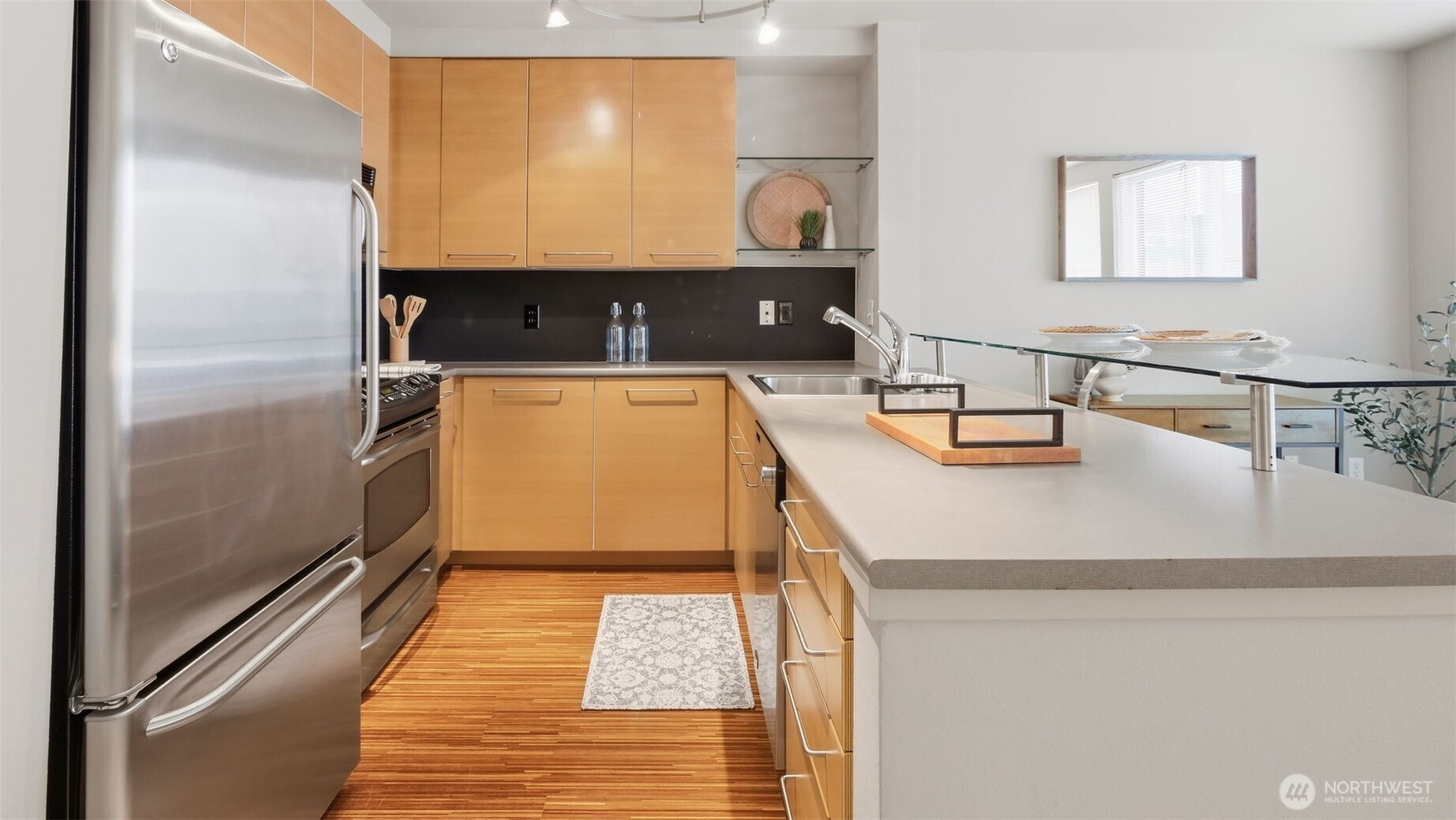 Modern condo kitchen with light wood cabinets, stainless steel appliances, and a wide peninsula with a sink.