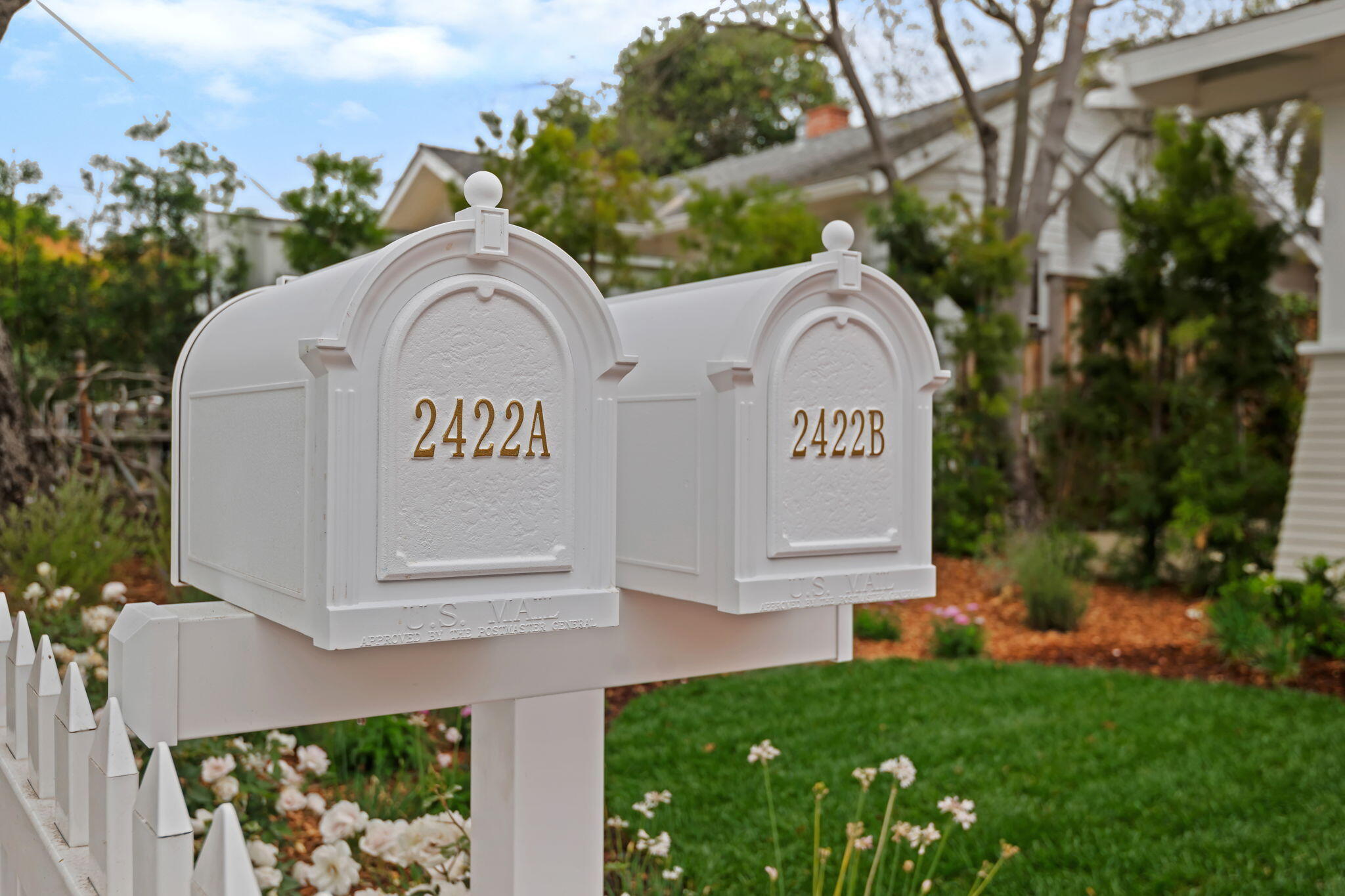 Two white mailboxes labeled 2422A and 2422B stand beside a picket fence and garden.