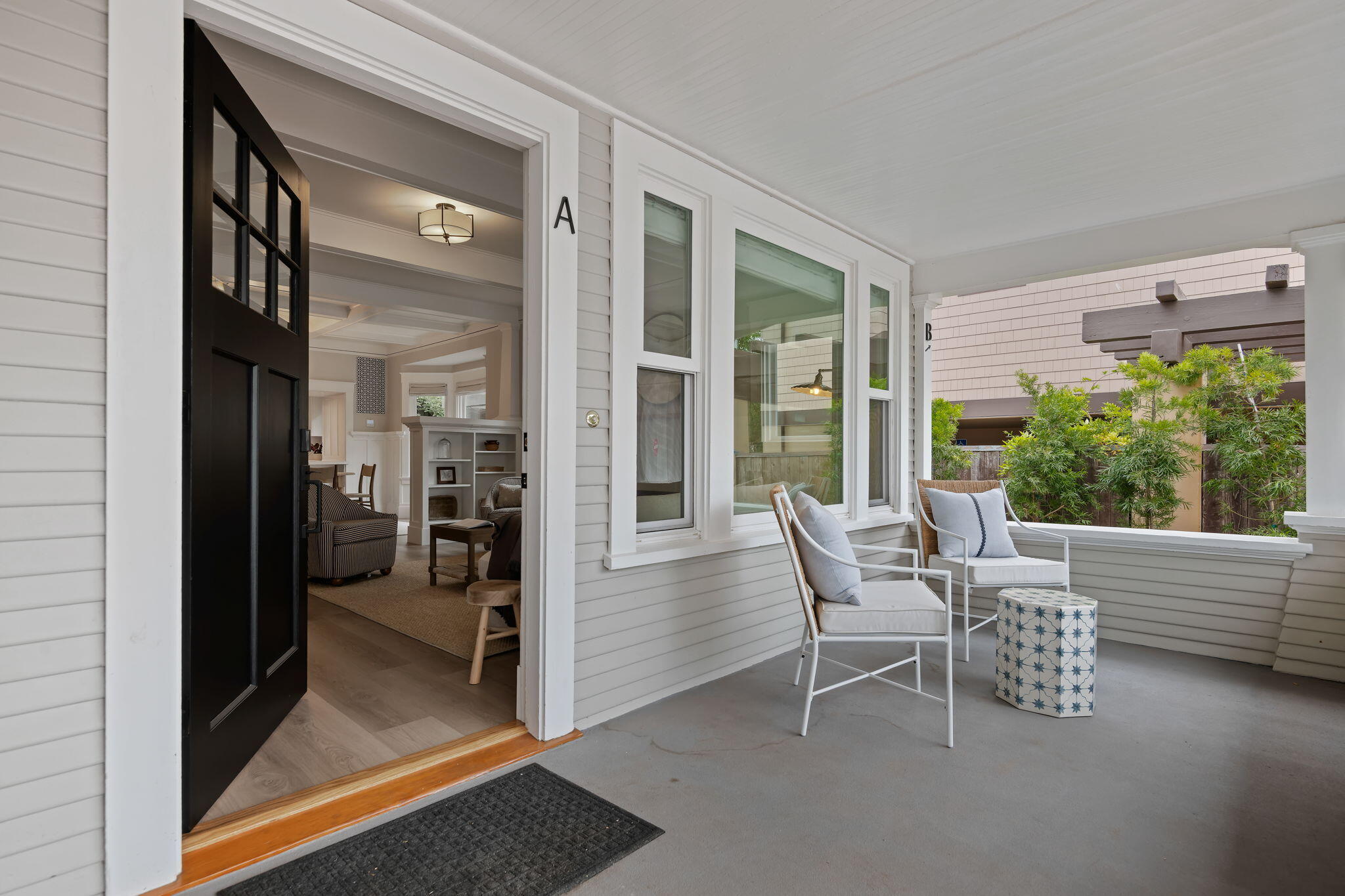 Covered porch with two cushioned chairs outside an open black door marked A; the living room is visible inside.