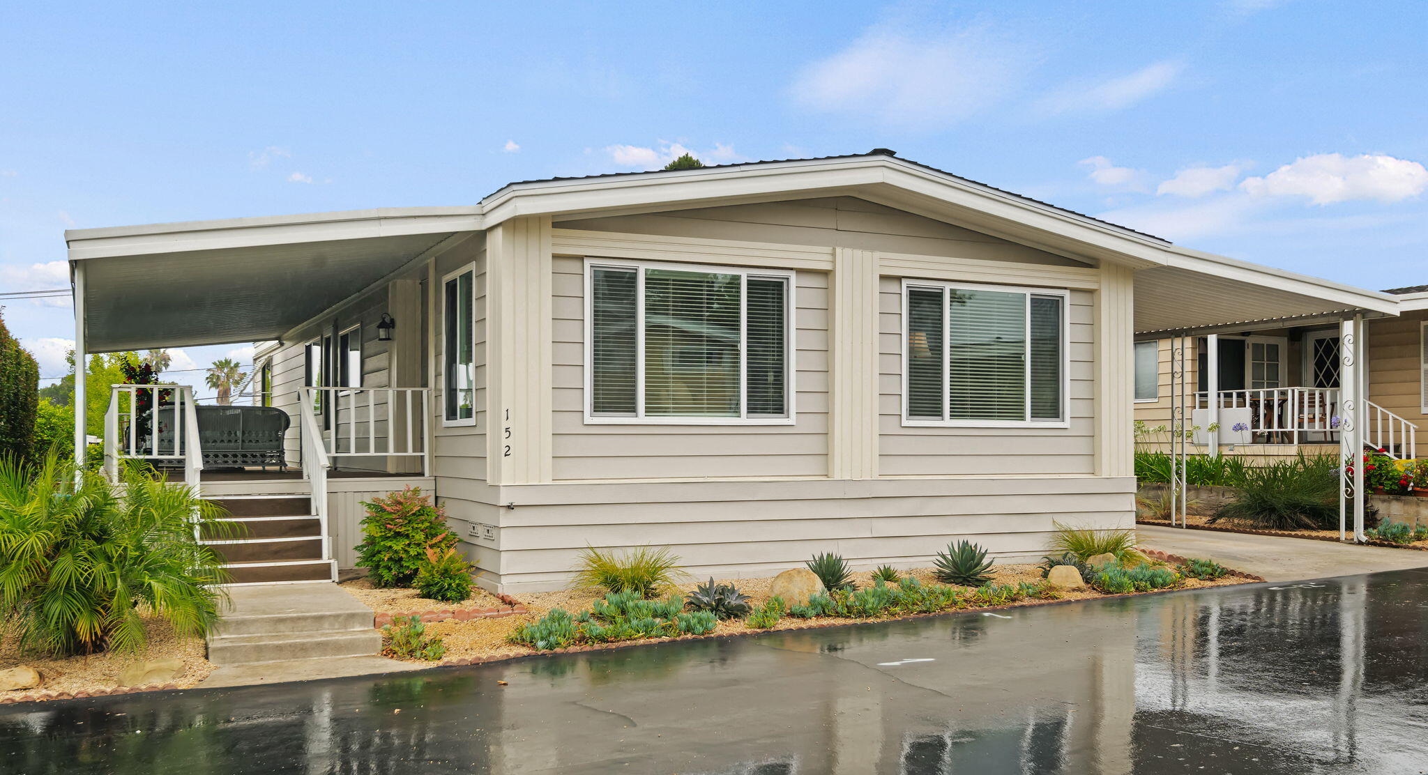 Beige manufactured home with a broad peaked roof, covered porch, porch swing, and succulent landscaping.