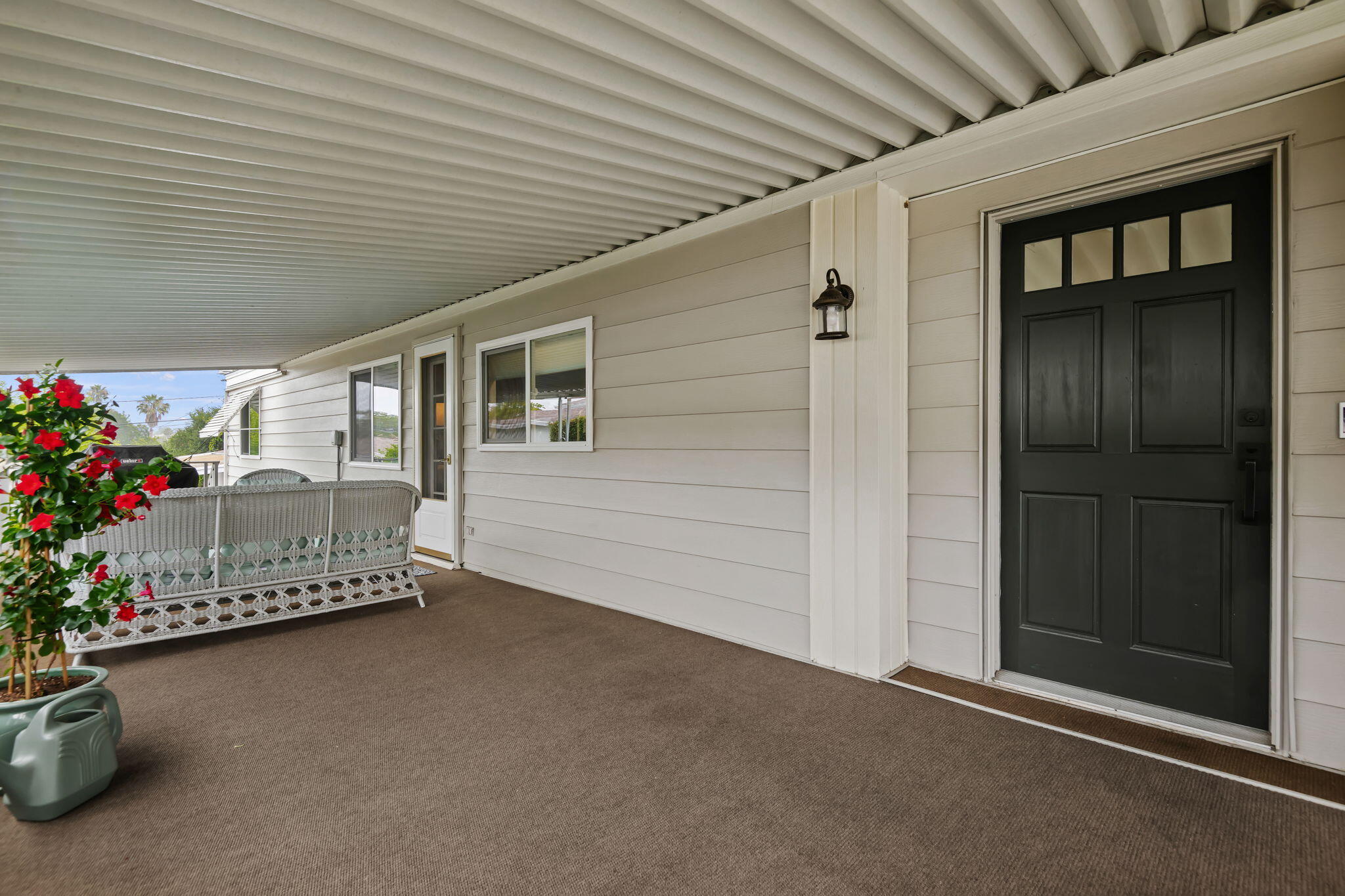 Covered porch with a black front door, wicker bench, and red flowers.