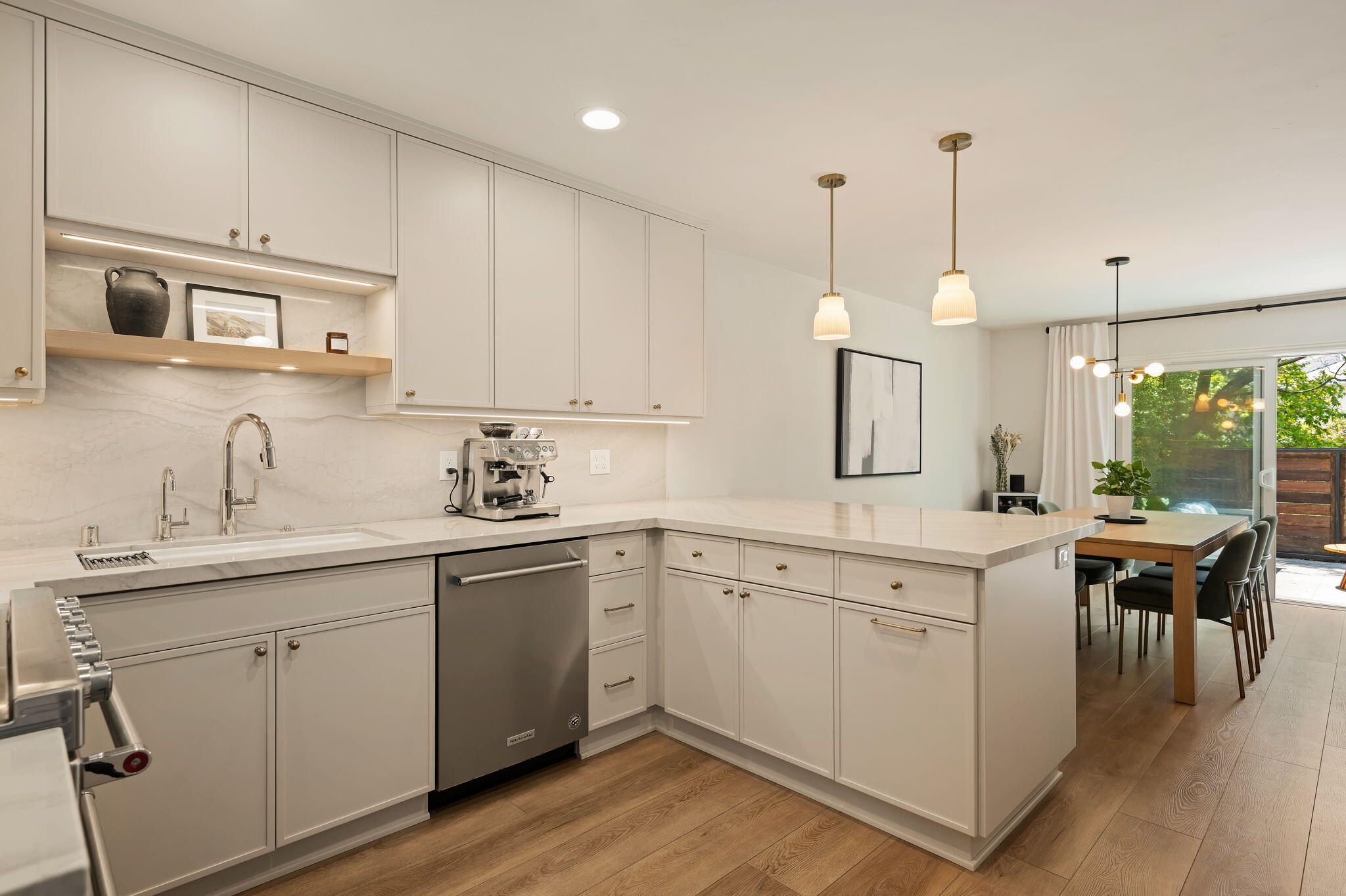 Modern white kitchen with a large island, stainless steel appliances, and dining area opening to a patio.