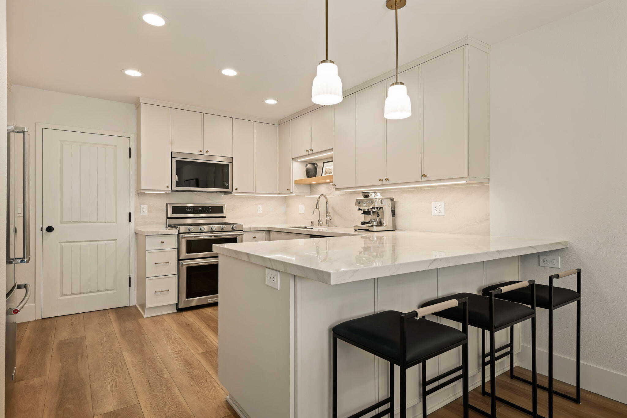 Renovated white kitchen with stainless steel appliances, a large peninsula, and black bar stools.