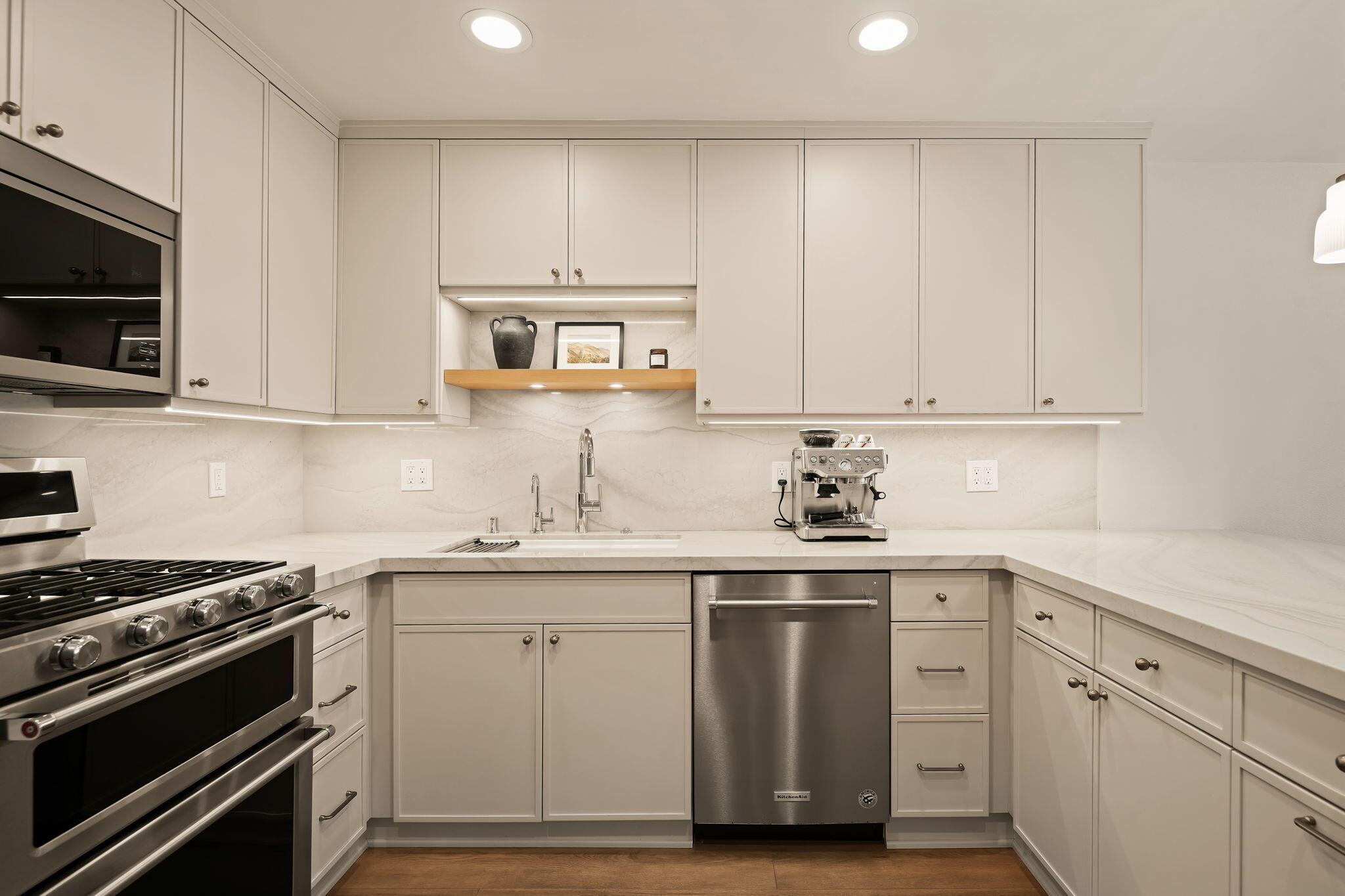 Kitchen with white cabinetry, marble counters, stainless steel appliances, and a built-in espresso machine.