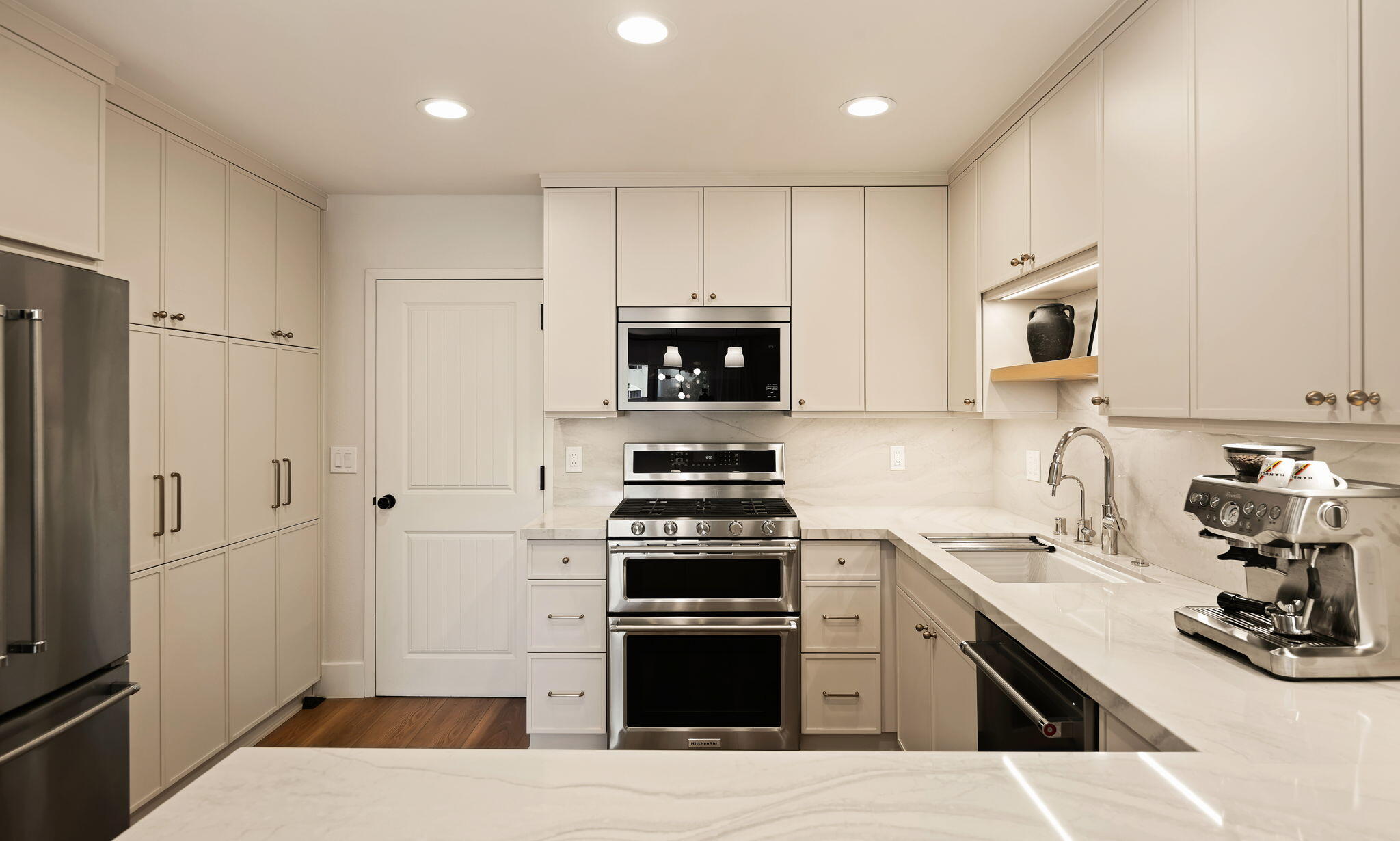 Kitchen with white cabinetry, marble counters, stainless steel appliances, and a double oven.