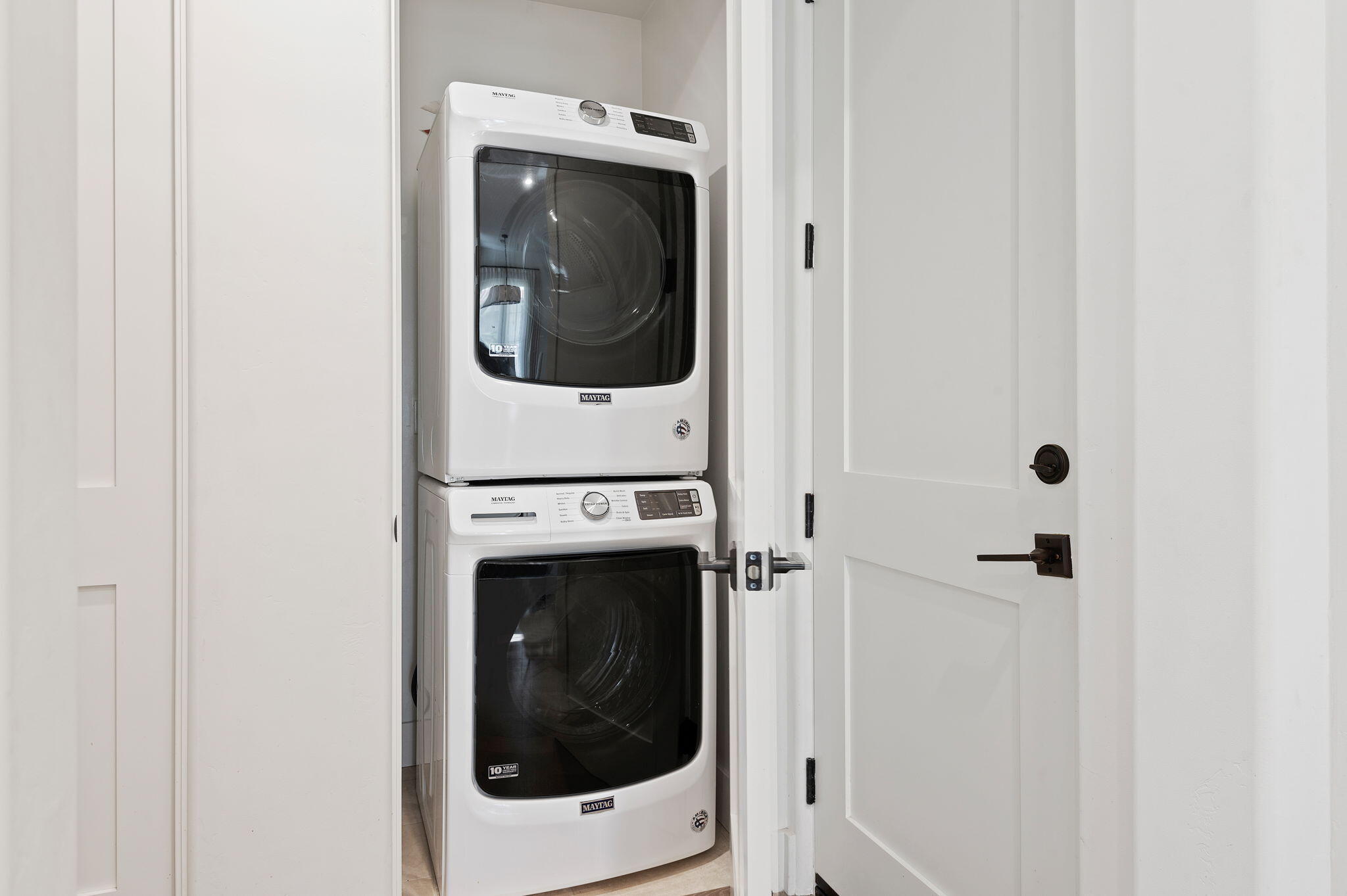 Stacked white Maytag washer and dryer in a closet behind an open paneled door.