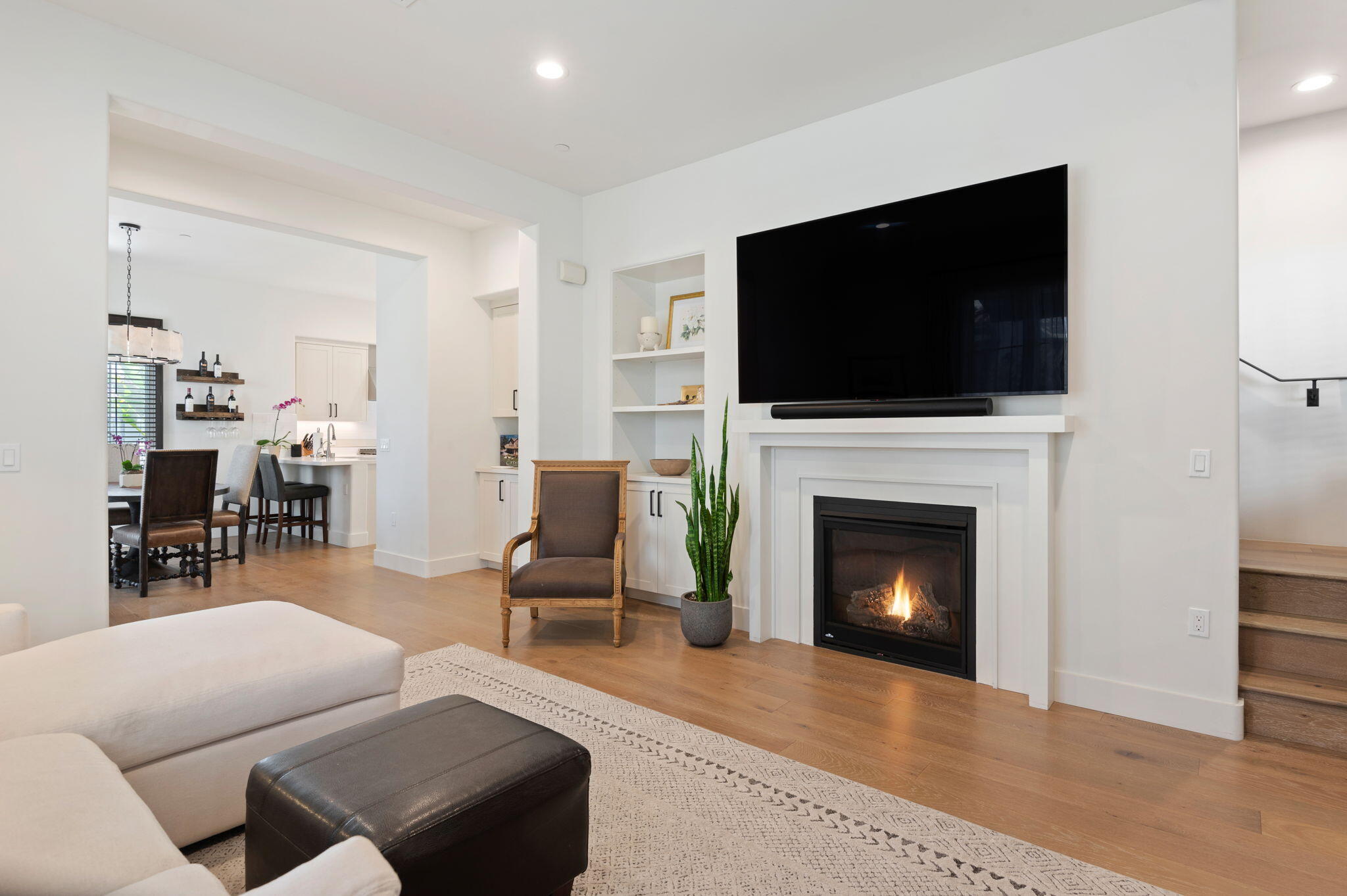 Living room with a lit fireplace, large television, white sectional, and view into the kitchen and dining area.