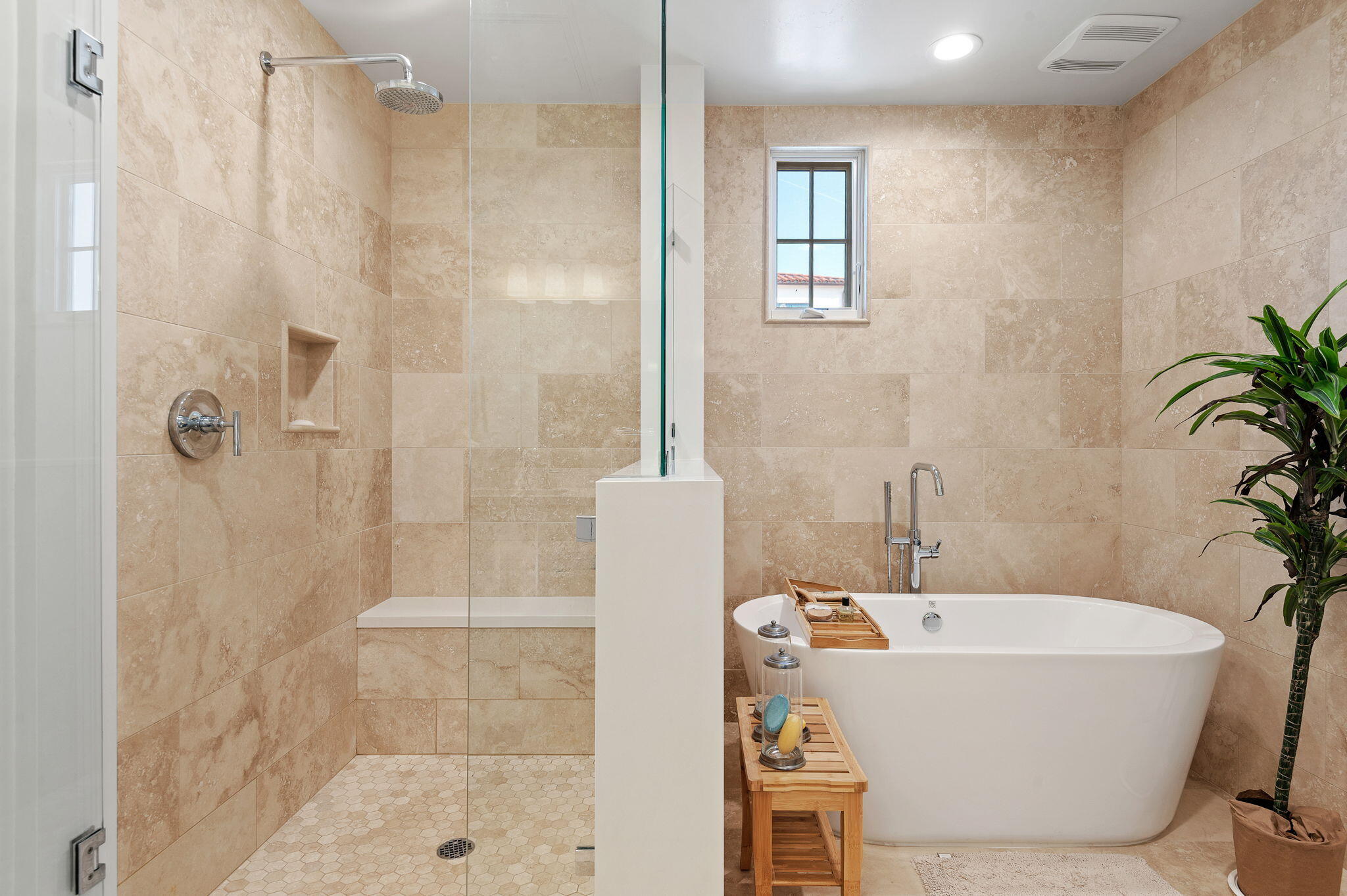 Bathroom with a glass walk-in shower and freestanding soaking tub against beige stone tile.