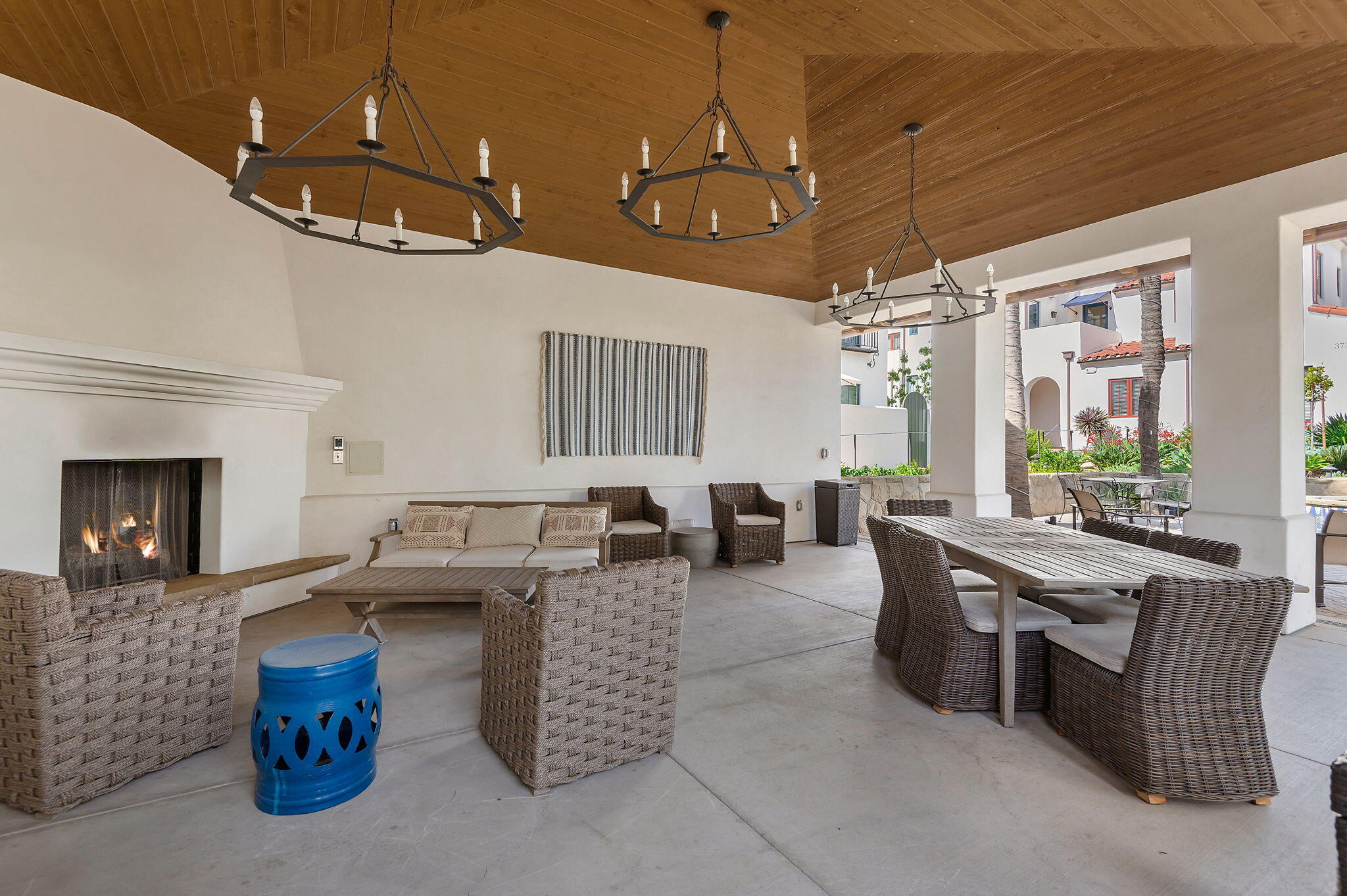Covered patio with a wood ceiling, lit fireplace, wicker seating, and courtyard views.